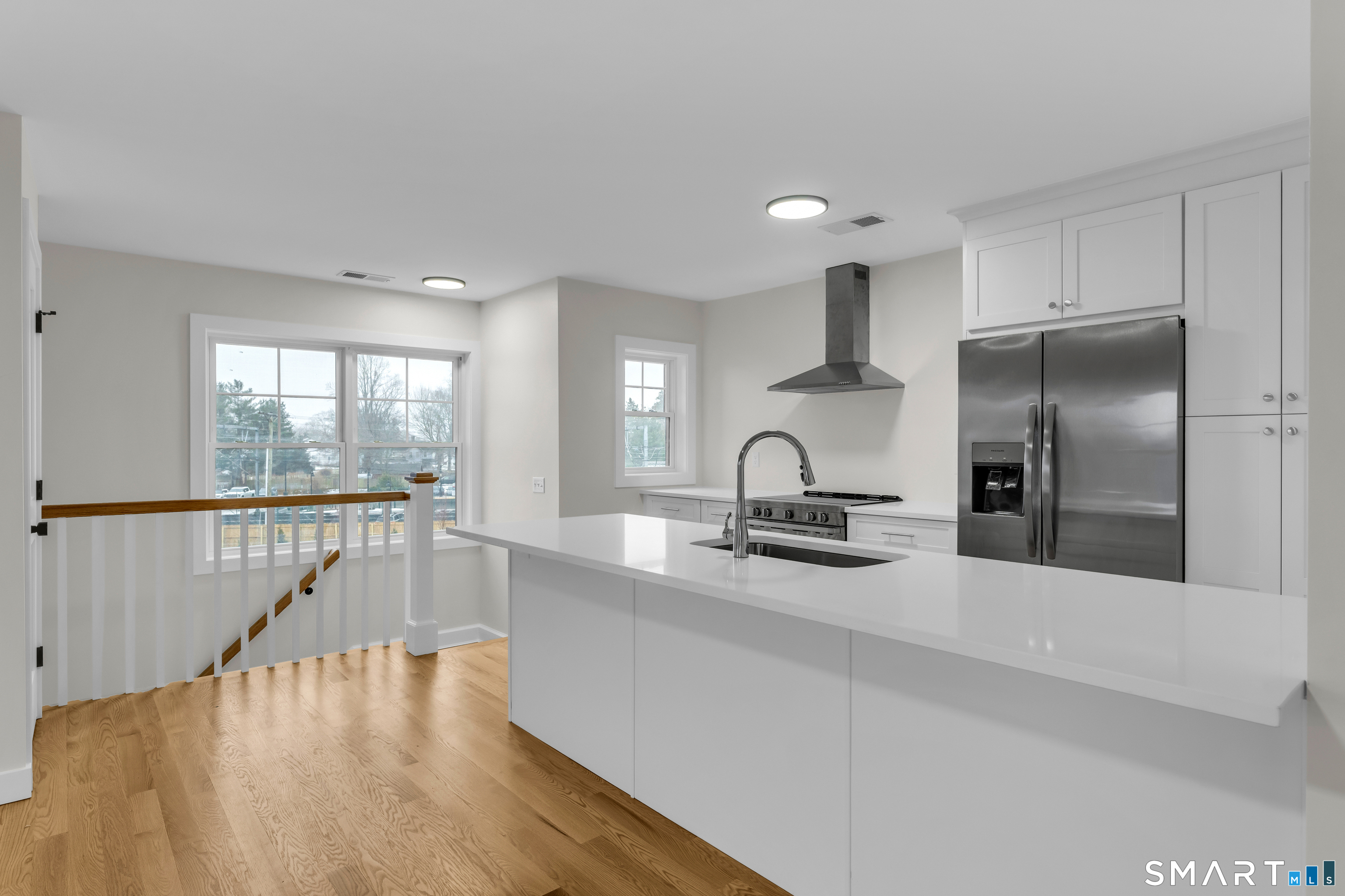 a kitchen with stainless steel appliances granite countertop a refrigerator a sink a stove and white cabinets with wooden floor