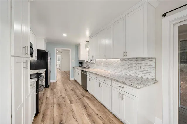 a large kitchen with a stove a sink dishwasher a refrigerator and white cabinets with wooden floor