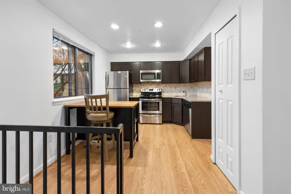 a open kitchen with stainless steel appliances granite countertop a stove top oven a sink dishwasher a dining table and chairs with wooden floor