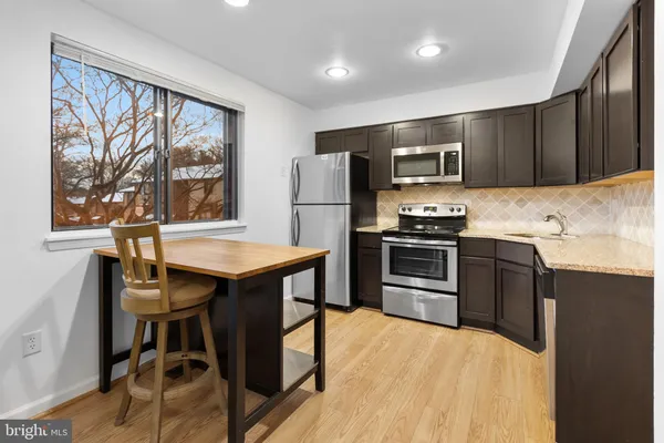 a kitchen with stainless steel appliances granite countertop a stove a refrigerator a sink a dining table and chairs