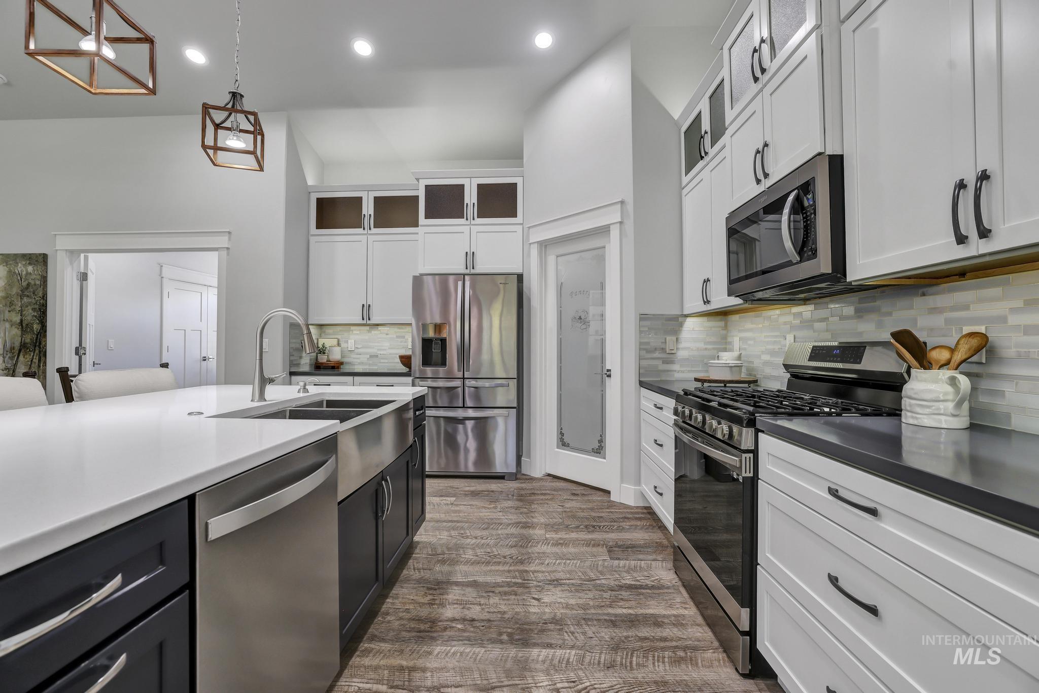 1937 Tamarack Loop Twin Falls, ID 83301 - Photo 14 of 50 Kitchen featuring a spacious island with an undermount double-basin sink, stainless steel appliances, white cabinetry, dark countertops, and wood-finish flooring