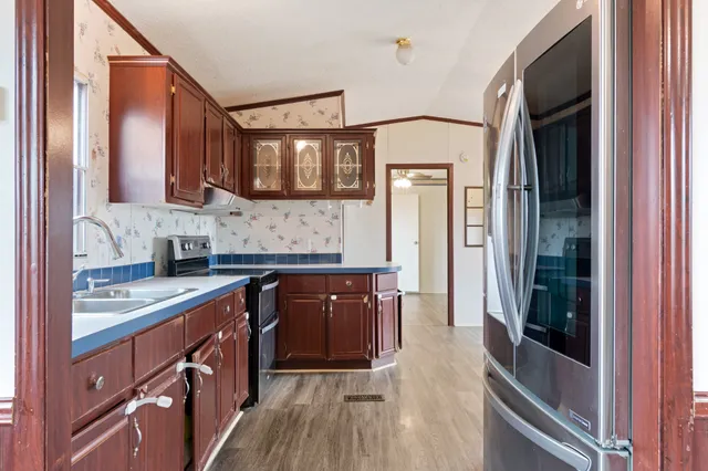 a kitchen with stainless steel appliances granite countertop a refrigerator a sink dishwasher a stove and white countertops with wooden floor