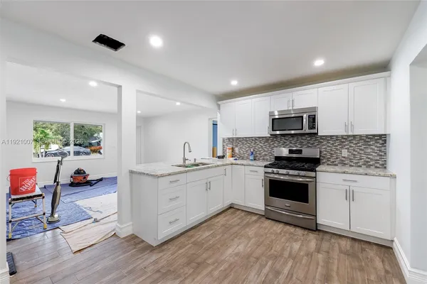 a kitchen with stainless steel appliances white cabinets a sink dishwasher a stove and a refrigerator with wooden floor