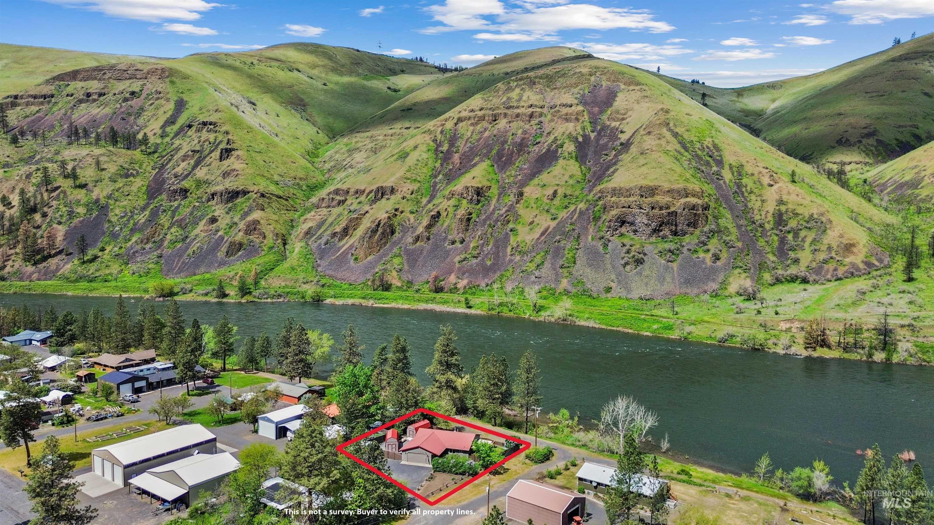 20015 Clark Street Juliaetta, ID 83535 - Photo 2 of 46 Residential property featuring a red roof and surrounding greenery, situated by a river with mountainous terrain forming a natural backdrop