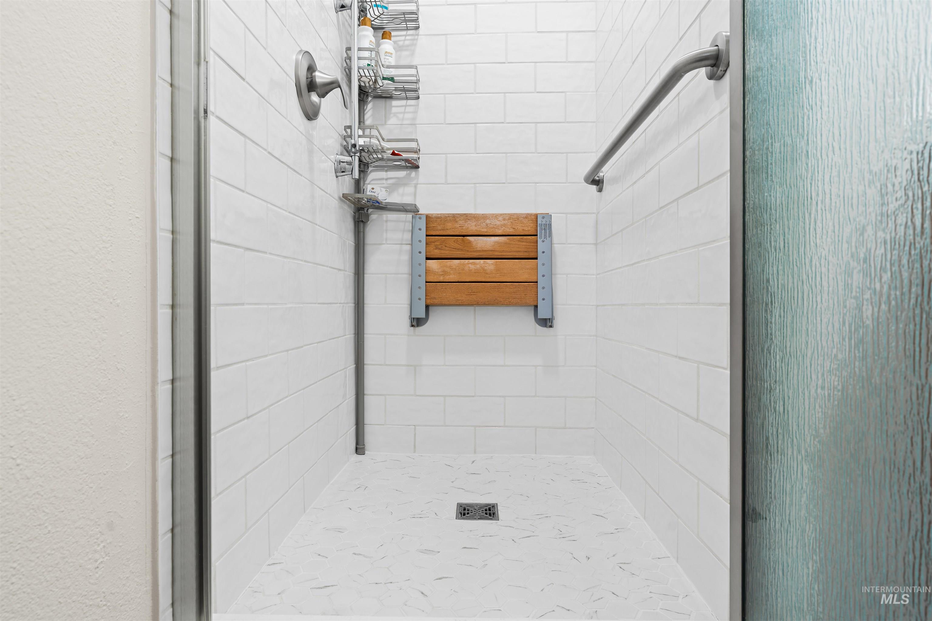20015 Clark Street Juliaetta, ID 83535 - Photo 21 of 46 Shower stall featuring white subway tile, a folding wood-finish seat, a polished chrome grab bar, and textured glass enclosure