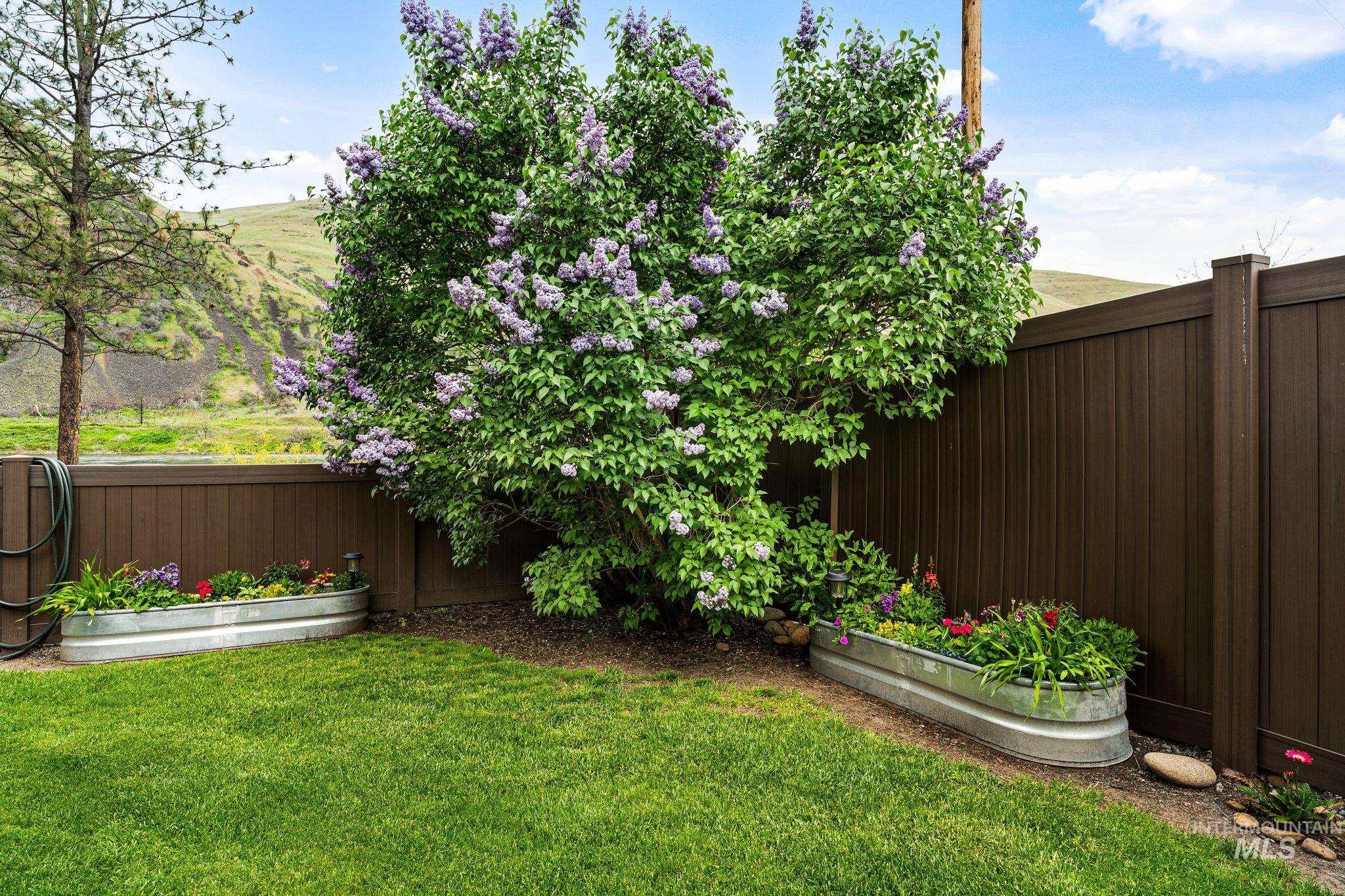 20015 Clark Street Juliaetta, ID 83535 - Photo 43 of 46 Landscaped yard featuring a blooming lilac bush, two galvanized metal raised garden beds with plantings, and a dark brown privacy fence