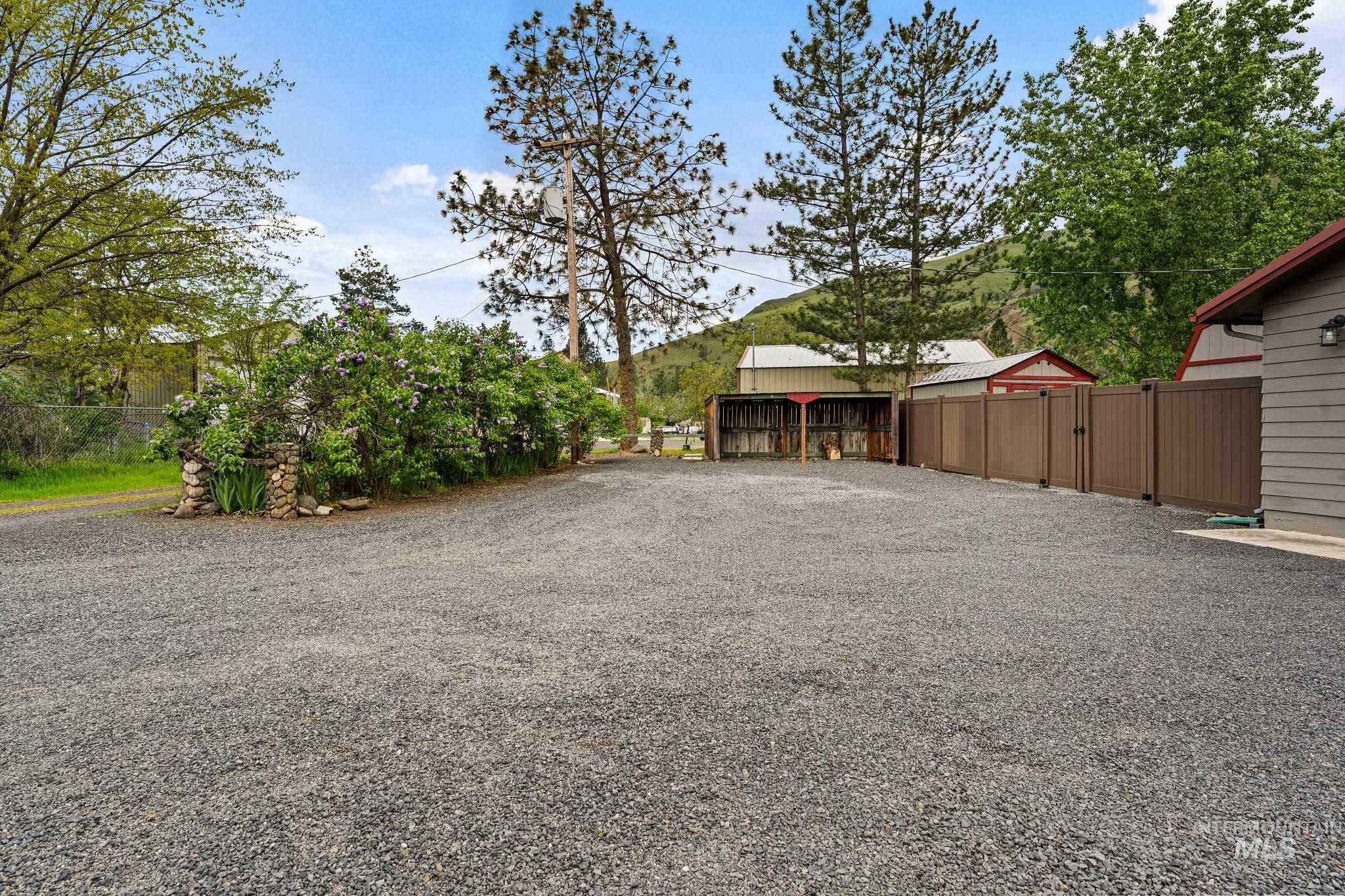 20015 Clark Street Juliaetta, ID 83535 - Photo 46 of 46 Expansive gravel parking area bordered by a brown privacy fence, a stone pillar, and mature trees