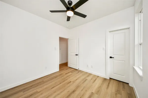 an empty room with wooden floor ceiling fan and windows
