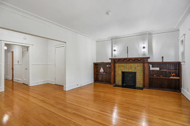 a view of an empty room with wooden floor and a fireplace