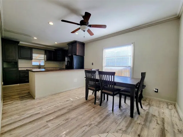 a kitchen with stainless steel appliances granite countertop a stove top oven a refrigerator a dining table and chairs with wooden floor