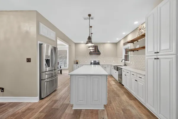 a kitchen with stainless steel appliances kitchen island granite countertop a refrigerator a sink dishwasher a oven with white cabinets and wooden floor