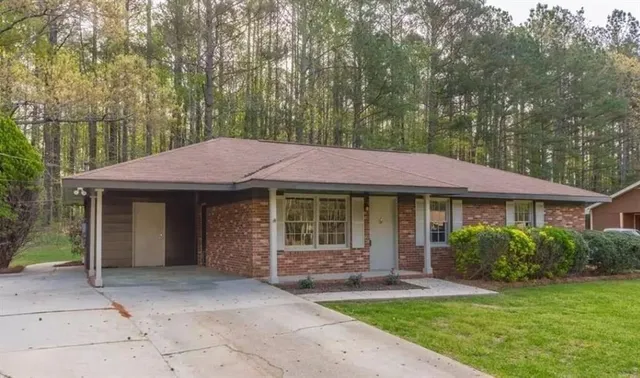 a view of a house with a yard plants and large tree