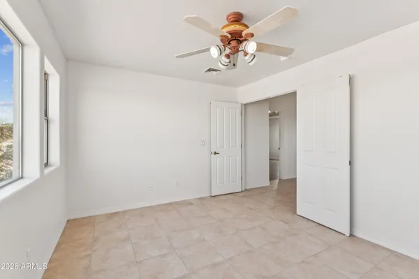 an empty room with a chandelier fan and kitchen view