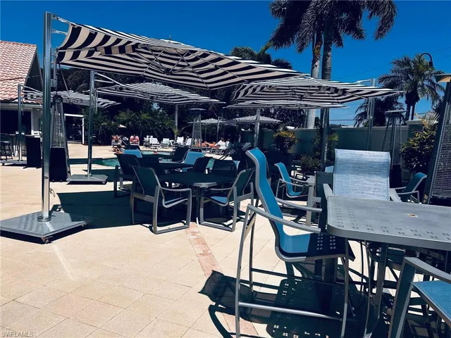 a view of a patio with dining table and chairs under an umbrella with a barbeque