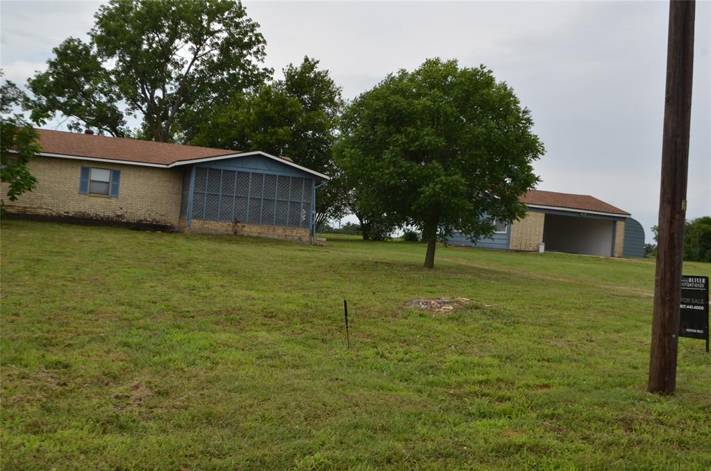2020 Gage Road Cleburne, TX 76031 - Photo 2 of 12 Two-structure property featuring a tan exterior residence with blue window shutters and a screened porch, alongside a blue and tan accessory building with an open bay