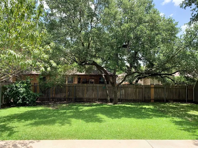 a view of a backyard with large trees and wooden fence