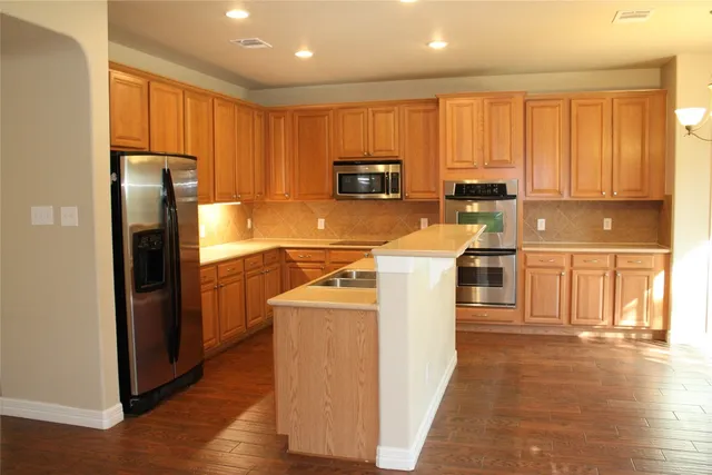 a kitchen with stainless steel appliances granite countertop a refrigerator a stove top oven a sink and dishwasher with wooden floor