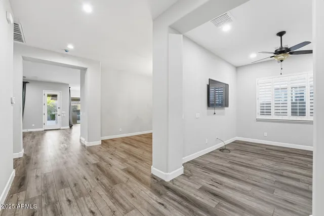a view of an empty room with wooden floor and a ceiling fan