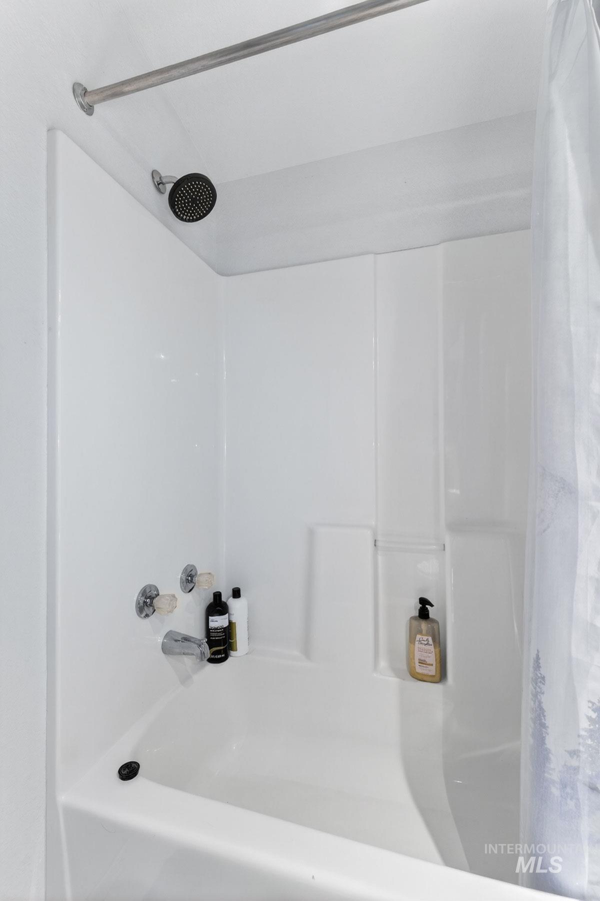 151 Cow Creek Road Lucile, ID 83542 - Photo 33 of 50 White acrylic tub and shower combination featuring a dark finish shower head, chrome fixtures, and a shower rod