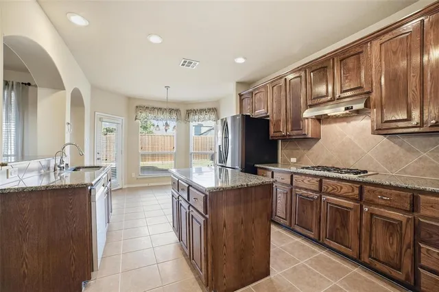 a kitchen with stainless steel appliances granite countertop a stove top oven a sink dishwasher and a refrigerator with wooden cabinets