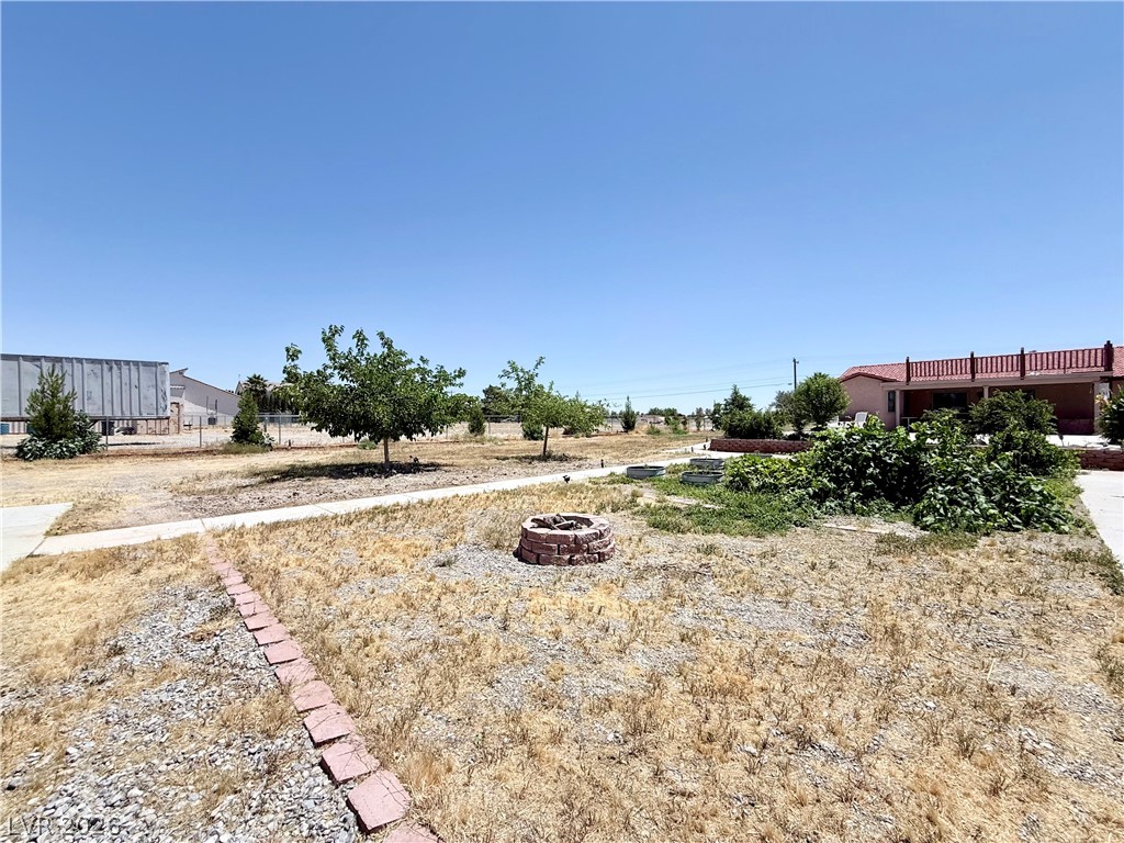 1220 East Gamebird Road Pahrump, NV 89048 - Photo 24 of 49 A spacious backyard awaits, featuring a charming fire pit and mature landscaping.