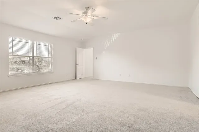 an empty room with chandelier fan and windows