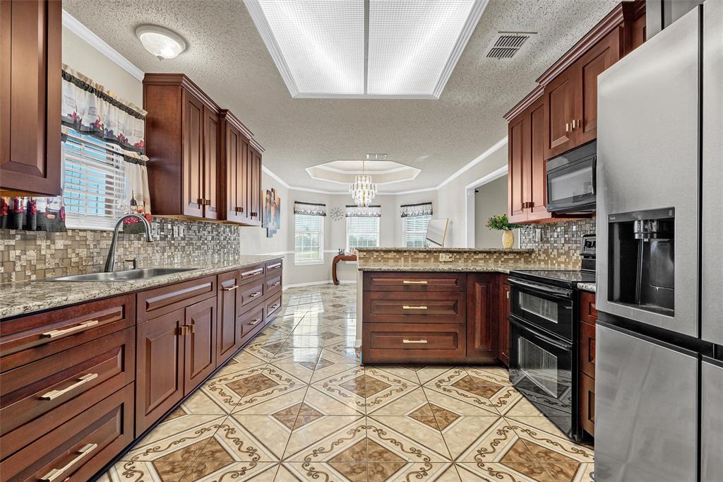494 Westgate I Road Eddy, TX 76524 - Photo 11 of 34 Kitchen with black appliances, crown molding, a textured ceiling, a peninsula, and light stone countertops