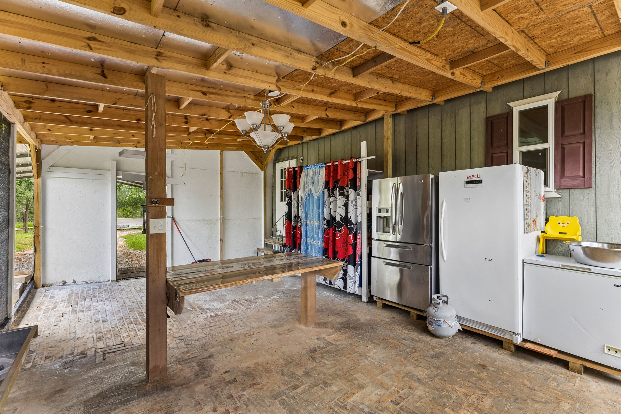 253 North County Line Road, Unit C Elgin, TX 78621 - Photo 24 of 39 An open-air utility area features rustic wood beams and a brick-patterned floor, providing a versatile space.
