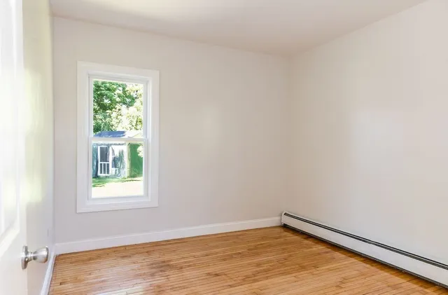 a view of an empty room with wooden floor and a window