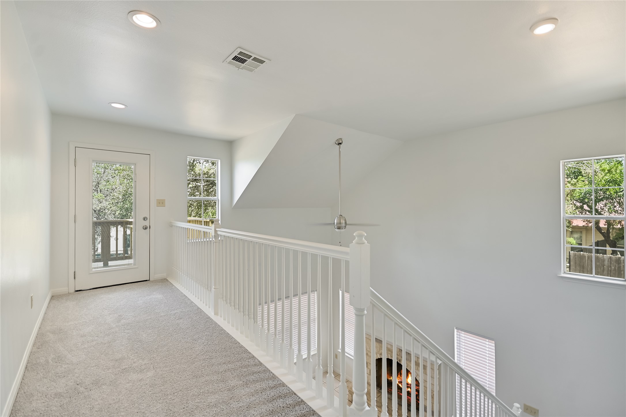 104 Crazy Cross Road Wimberley, TX 78676 - Photo 9 of 20 A loft hallway features carpeted flooring and white railings overlooking the lower level fireplace.