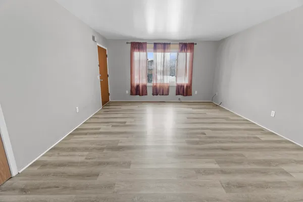 a view of an empty room with wooden floor and a window