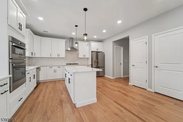 a kitchen with stainless steel appliances granite countertop a refrigerator a sink dishwasher a stove and white countertops with wooden floor