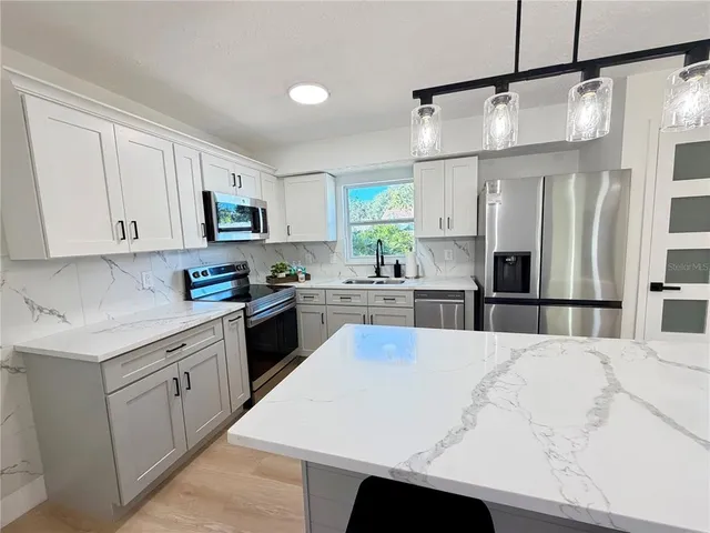 a kitchen with stainless steel appliances kitchen island granite countertop a refrigerator a sink dishwasher a stove and white cabinets with wooden floor