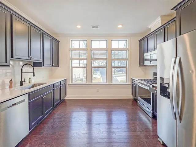 a large kitchen with stainless steel appliances granite countertop a refrigerator a sink dishwasher a stove and a refrigerator with wooden floor