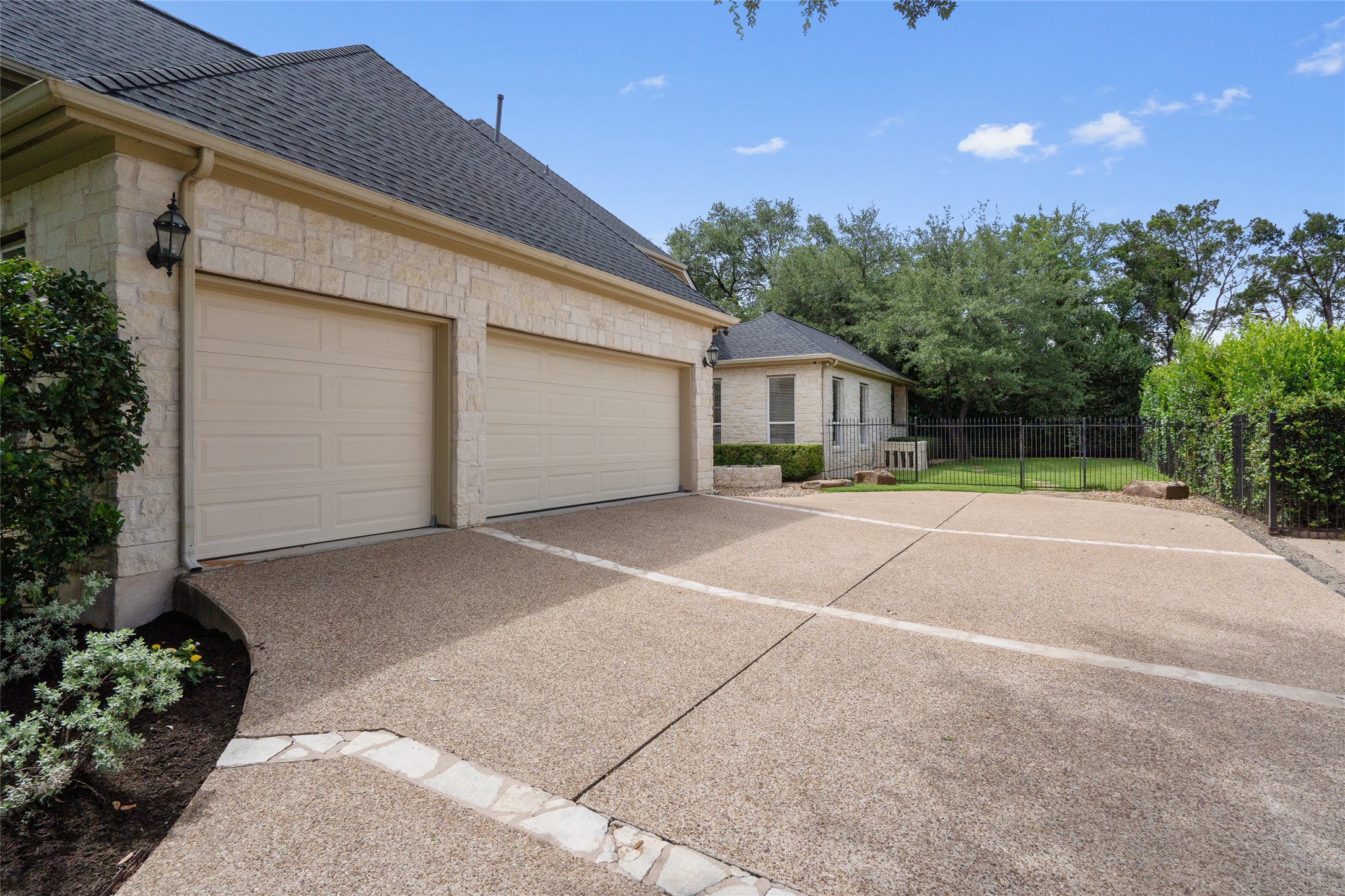 4313 Rio Robles Drive Austin, TX 78746 - Photo 3 of 40 A textured concrete driveway leads to a two-car garage with stone veneer accents.