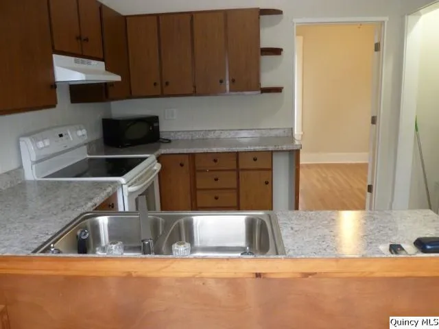 a kitchen with stainless steel appliances granite countertop a sink a stove and a refrigerator with wooden cabinets