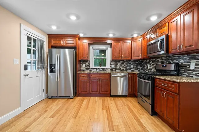 a kitchen with stainless steel appliances granite countertop a refrigerator a sink dishwasher a stove with wooden cabinets and floor