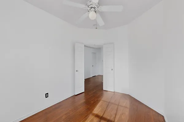 a view of an empty room with wooden floor and a ceiling fan