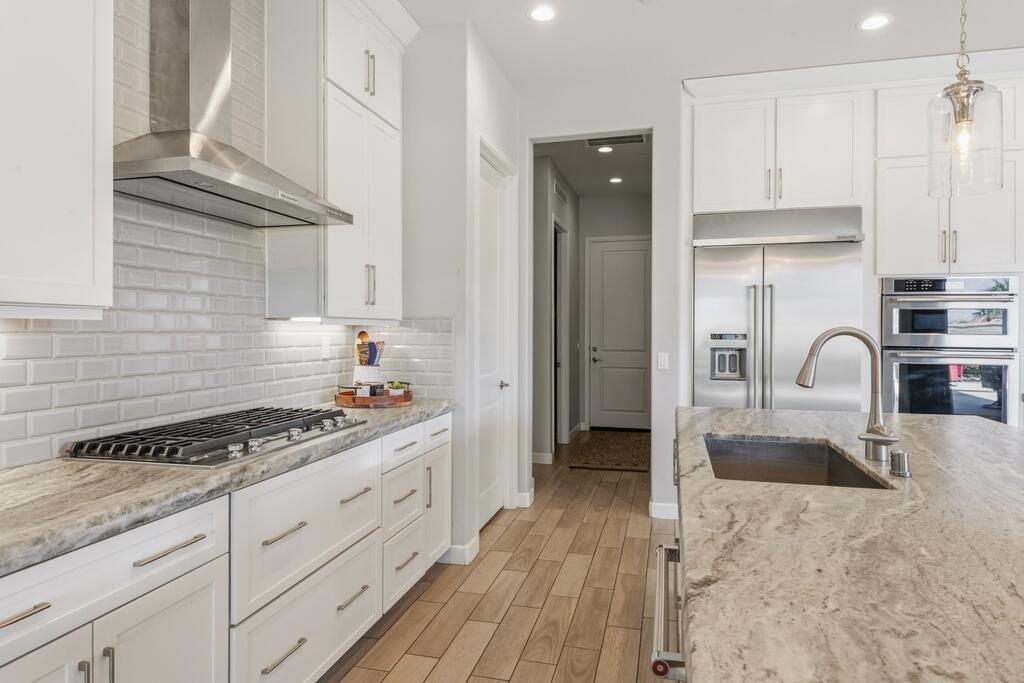 77 Barolo Rancho Mirage, CA 92270 - Photo 28 of 61 a kitchen with granite countertop a stove a sink dishwasher and white cabinets with wooden floor