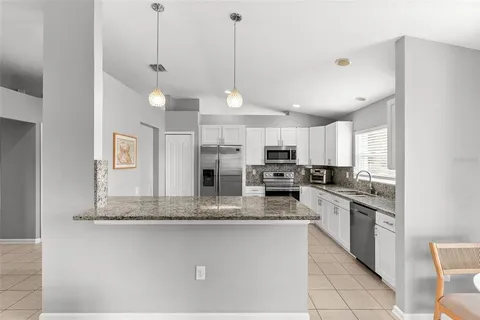 a kitchen with stainless steel appliances granite countertop a sink a stove a refrigerator and white cabinets