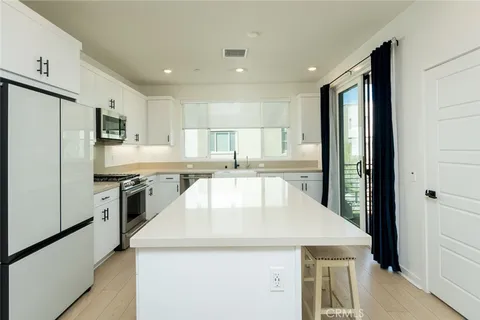 a kitchen with kitchen island a stove a sink a refrigerator and white cabinets with wooden floor