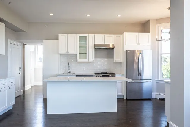 a kitchen with stainless steel appliances granite countertop a refrigerator a sink a stove and white cabinets with wooden floor