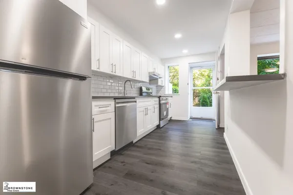 a kitchen with stainless steel appliances granite countertop a refrigerator a sink a stove and white cabinets with wooden floor