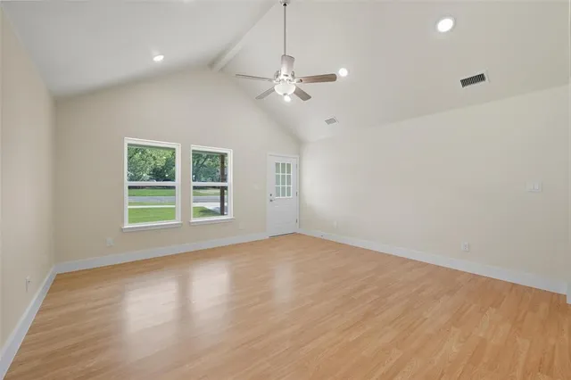 an empty room with wooden floor chandelier fan and windows