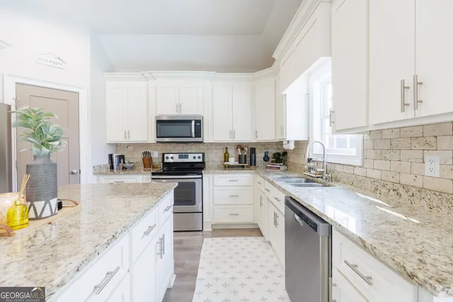 a kitchen with granite countertop a sink stainless steel appliances and white cabinets
