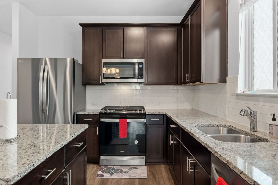 1600 Hope Rnch Road Leander, TX 78641 - Photo 4 of 29 Kitchen featuring stainless steel appliances, dark brown cabinets, light stone countertops, island and tasteful backsplash