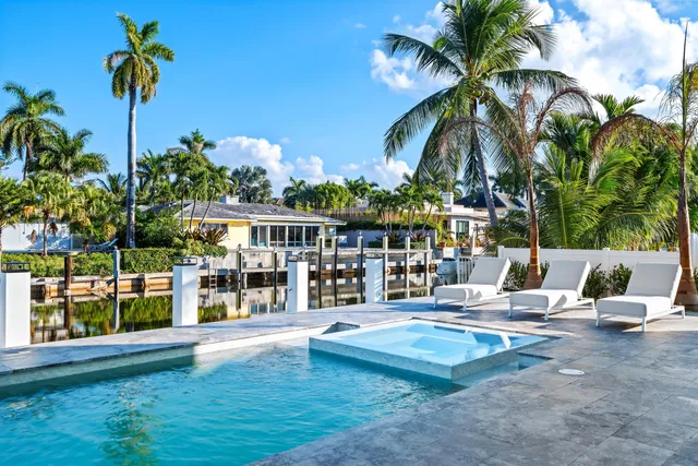 a view of swimming pool with lawn chairs plants and palm trees
