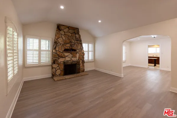 an empty room with wooden floor fireplace and windows