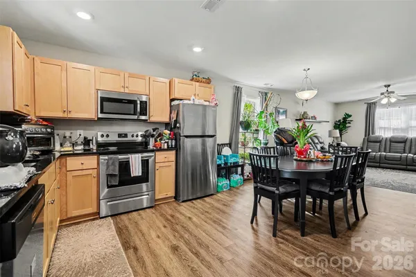 a kitchen with stainless steel appliances granite countertop a stove a refrigerator a kitchen island a dining table and chairs with wooden floor