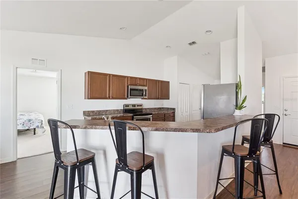 a kitchen with stainless steel appliances kitchen island granite countertop a dining table chairs and a refrigerator